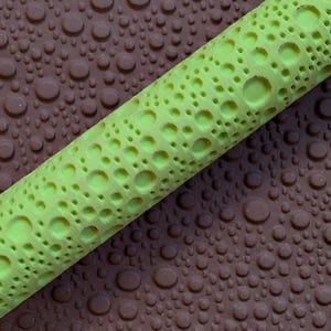 May include: A close-up of a neon green cylindrical object with a textured surface. The object is diagonally positioned against a brown background covered in small, round, water-like droplets.