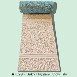 May include: A light blue patterned roller sits atop a cream-colored tile, both featuring floral and animal designs. The tile is rectangular with a detailed relief pattern of a Highland cow and floral elements. The text "#1029 - Baby Highland Cow Tile" is at the bottom.