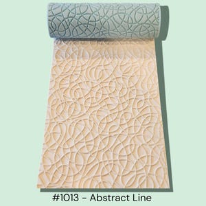 May include: A textured rolling pin with an abstract line design, unrolled on a matching surface. The rolling pin is a light teal color, and the surface is a light beige. The text "#1013 - Abstract Line" is at the bottom.
