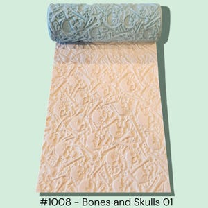 May include: A light blue textured roller with a repeating skull and bone pattern, unrolled onto a beige surface with the same design. The text "#1008 - Bones and Skulls 01" is at the bottom.
