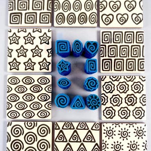May include: A collection of eleven blue foam stamps with various geometric and spiral patterns, surrounded by twelve square white tiles featuring black printed designs including hearts, stars, spirals, triangles, and sun-like motifs.