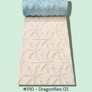 May include: A light blue patterned roller with a dragonfly design, creating an embossed pattern on a cream-colored surface. The roller is at the top, with the embossed pattern extending below. The text at the bottom reads "#1110 - Dragonflies 02".