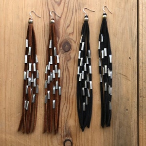 May include: A pair of long, brown suede earrings with silver beads and a pair of long, black suede earrings with silver beads.