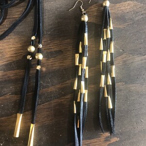 May include: A pair of long black leather earrings with gold accents. The earrings are made of multiple strands of leather with gold tips.