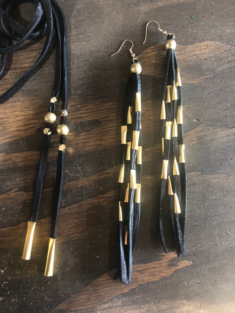 May include: A pair of long black leather earrings with gold accents. The earrings are made of multiple strands of leather with gold tips.