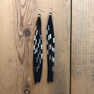 May include: A pair of long black suede earrings with silver metal accents. The earrings are dangling and have a fringe-like design.