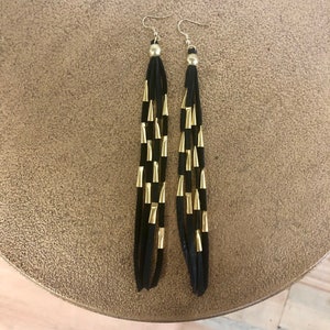 May include: A pair of long black tassel earrings with gold accents. The earrings are made of suede and have a simple design.