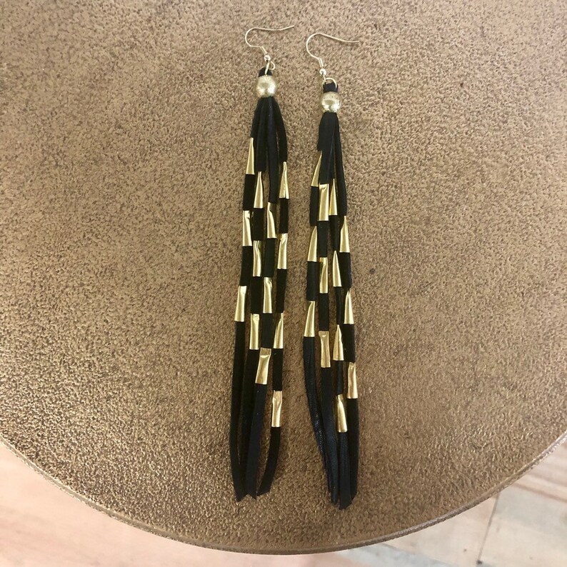 May include: A pair of long black tassel earrings with gold accents. The earrings are made of suede and have a simple design.