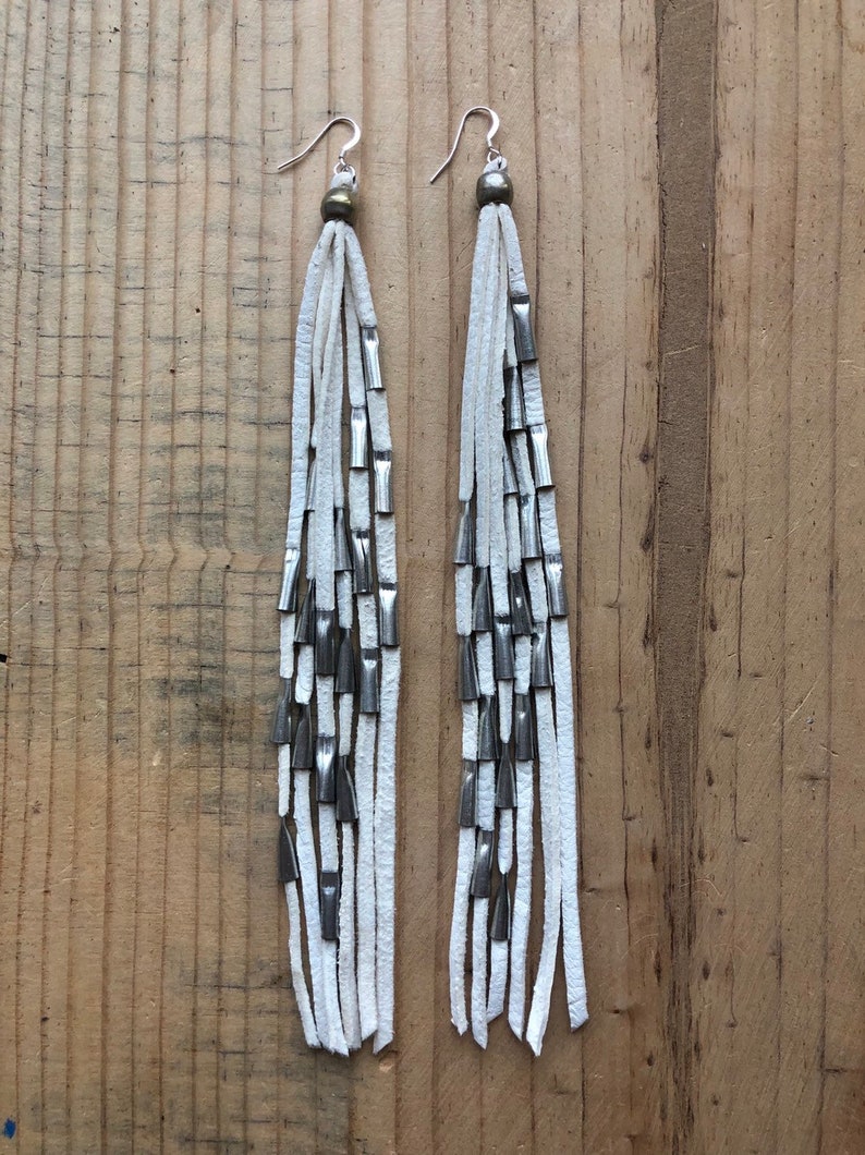 May include: White leather earrings with silver metal accents. The earrings are long and dangle, with multiple strands of leather and metal beads.
