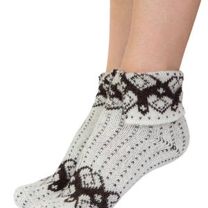 Puede incluir: Calcetines blancos de punto con un patrón geométrico marrón. Los calcetines tienen un puño doblado y un diseño repetido en el pie. Fabricados con un material suave y cálido.