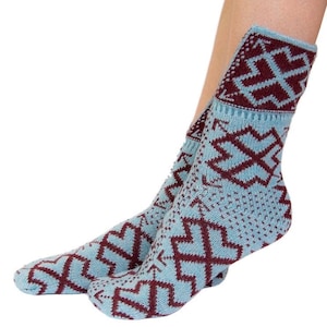 Puede incluir: Un par de calcetines azul claro con un patrón geométrico granate. Los calcetines son hasta la rodilla y presentan un diseño repetido de cruces estilizadas y otras formas. Los calcetines están hechos de material de punto.