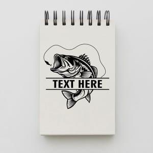 May include: A spiral-bound notepad with a black and white illustration of a largemouth bass with a hook in its mouth. The text "TEXT HERE" is displayed in a horizontal rectangle below the fish.