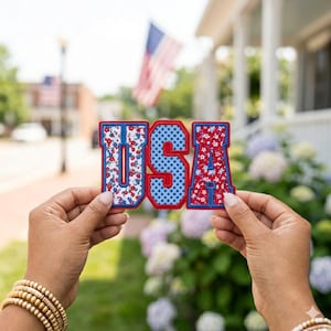 May include: The word "USA" in a collegiate-style font, each letter a separate patch. The letters are outlined in red with a blue border. The "U" and "A" have a floral pattern, while the "S" has a blue polka dot pattern.