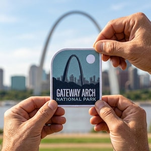 May include: A patch featuring the Gateway Arch National Park. The patch has a teal background with a white border. The arch is depicted in dark gray, with a cityscape silhouette below. The text "GATEWAY ARCH NATIONAL PARK" is displayed in white.