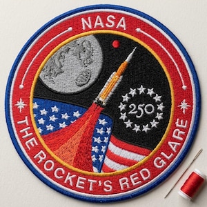 May include: Embroidered patch with a circular design featuring the NASA logo, a rocket launching towards a moon, and the text "THE ROCKET'S RED GLARE." The patch includes a blue, red, and white color scheme with the number "250" surrounded by stars.
