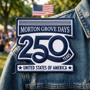 May include: A navy blue and white embroidered patch with the text "MORTON GROVE DAYS 250 YEARS UNITED STATES OF AMERICA" is affixed to a denim jacket. The American flag is visible in the background.