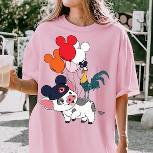 May include: Pink oversized t-shirt featuring a cartoon illustration of a pig wearing a hat and holding balloons shaped like Mickey Mouse. A rooster stands on the pig's back. The shirt is a solid pink color.