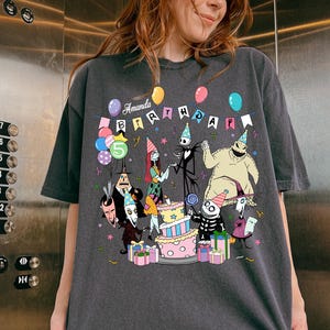Może przedstawiać: Ciemnoszara koszulka z kolorową grafiką postaci z Miasteczka Halloween świętujących urodziny. Koszulka ma napis "Amanda Birthday" i cyfrę "5". Widoczne są r&oacute;wnież balony i tort.