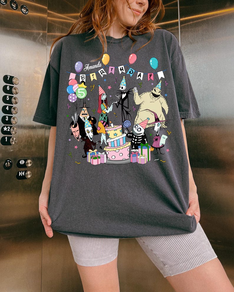 Może przedstawiać: Ciemnoszara koszulka z kolorową grafiką postaci z Miasteczka Halloween świętujących urodziny. Koszulka ma napis "Amanda Birthday" i cyfrę "5". Widoczne są r&oacute;wnież balony i tort.