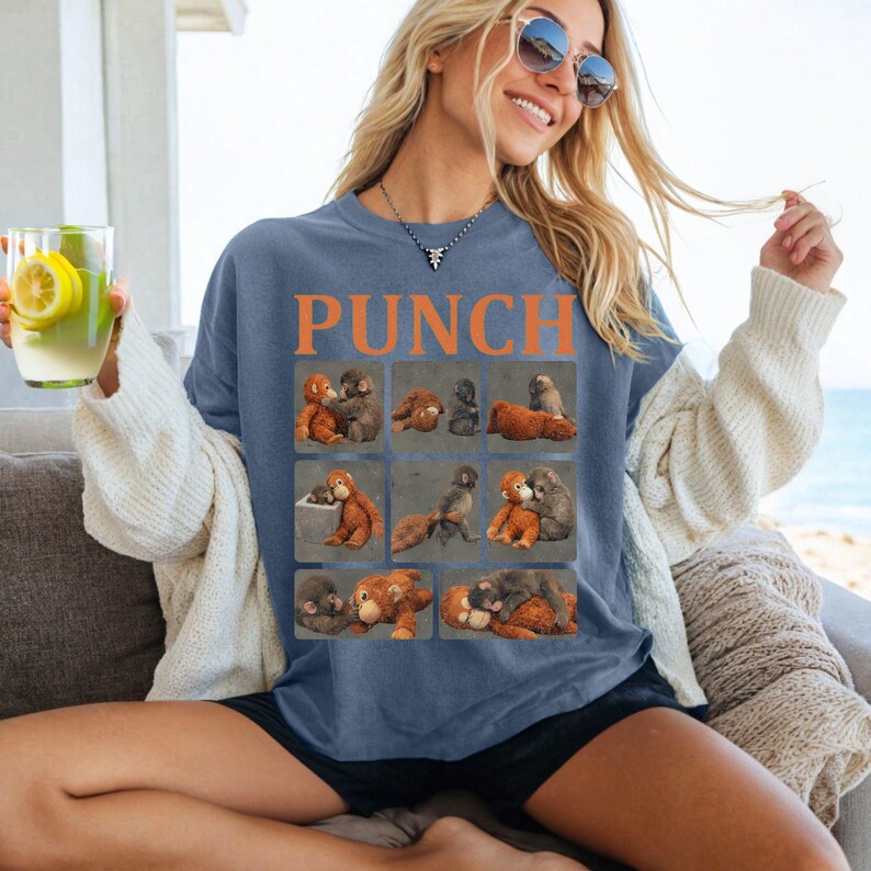 May include: A blue long-sleeve shirt with the word "PUNCH" in orange block letters. The shirt features a grid of nine illustrations of monkeys in various poses. The shirt is worn by a person sitting on a couch.