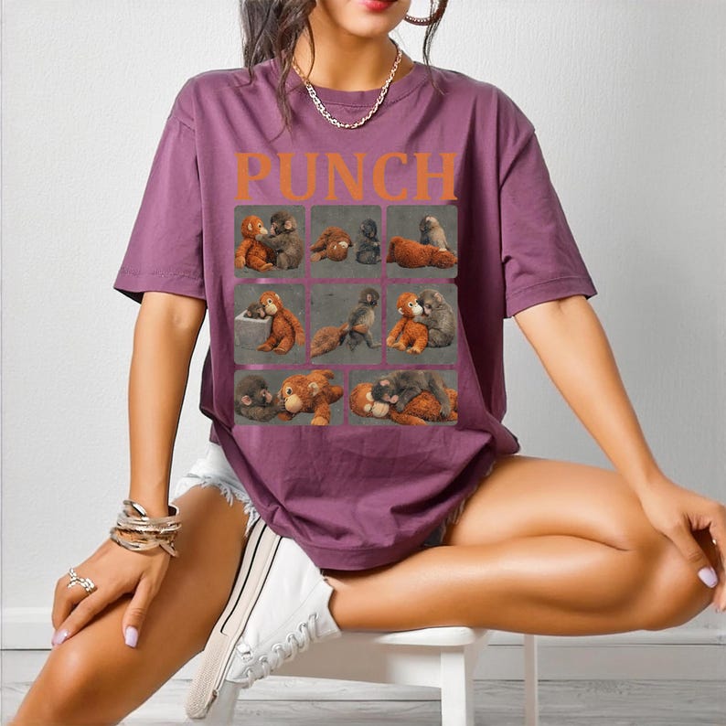 May include: A purple t-shirt with the word "PUNCH" in orange block letters. The shirt features a grid of nine squares, each containing a vintage illustration of teddy bears in various poses. The model is wearing white shorts and sneakers.