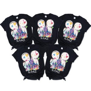 May include: Five black t-shirts with a colorful graphic of a castle inside a Mickey Mouse head shape. The design includes hearts and the word "NAME" at the bottom. The shirts are arranged in a fan shape.