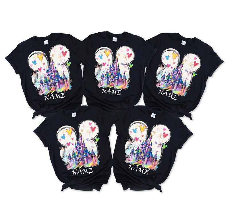 May include: Five black t-shirts with a colorful graphic of a castle inside a Mickey Mouse head shape. The design includes hearts and the word "NAME" at the bottom. The shirts are arranged in a fan shape.