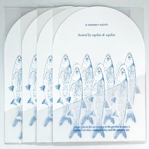 May include: A stack of white invitation cards with a blue fish illustration. The cards have a semi-circular top and are held in a clear plastic sleeve. Text reads "a summer soirée hosted by sophia & sophia".