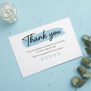May include: A white rectangular thank you card featuring a light blue brushstroke background behind the black text Thank you. Below, the text reads For your purchase and support to our business, You have made our day! We'd be very grateful for your review! with five light blue star outlines.