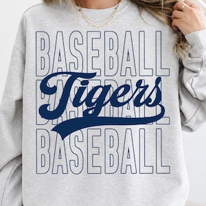 May include: A light grey sweatshirt featuring the text "BASEBALL Tigers BASEBALL" in navy blue. The word "Tigers" is in a script font. The sweatshirt has long sleeves and a crew neck.