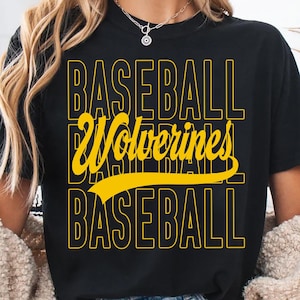 Op de afbeelding: Zwart T-shirt met de woorden "BASEBALL Wolverines BASEBALL" in gele blokletters. Het woord "Wolverines" is in een scriptlettertype. Het shirt heeft een ronde hals en korte mouwen.