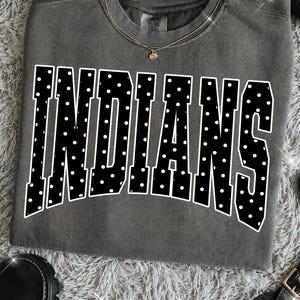 Könnte beinhalten: Ein anthrazitfarbenes Sweatshirt mit Rundhalsausschnitt und dem Wort INDIANS in großen, fetten, schwarzen Blockbuchstaben mit weißem Punktmuster. Das Kleidungsstück hat einen gerippten Halsausschnitt und ein Comfort Colors Etikett am Kragen.