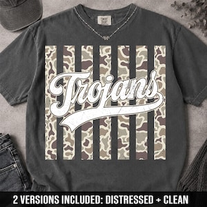 May include: A charcoal gray short-sleeve t-shirt featuring a central graphic of vertical stripes with a camouflage pattern. The word Trojans is printed in a large, white, script-style font across the center of the stripes. The shirt has a crew neckline.