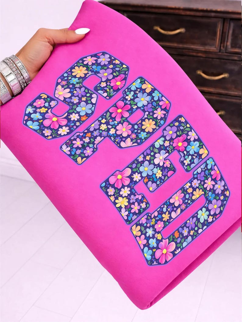Pode incluir: Tecido rosa vibrante com a palavra "SPED" num padr&atilde;o floral. As letras s&atilde;o contornadas em azul escuro e preenchidas com flores coloridas em tons de rosa, amarelo, azul e roxo. O tecido &eacute; segurado por uma m&atilde;o.