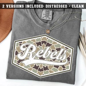 Könnte beinhalten: Ein anthrazitfarbenes T-Shirt mit einer sechseckigen Grafik in einem Tarnmuster in Grün-, Braun- und Beigetönen. Das Wort Rebels ist in großer, weißer Schreibschrift in der Mitte des Sechsecks gedruckt. Eine dünne silberne Halskette liegt auf dem Kragen.