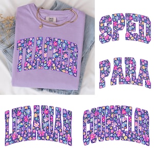 Op de afbeelding: Een lila Comfort Colors sweatshirt met het woord "TEACHER" in een bloemenontwerp. De afbeelding toont ook de woorden "SPED", "PARA", "LIBRARIAN" en "COUNSELOR" in een vergelijkbaar bloemenlettertype. Een gouden ketting ligt op het opgevouwen shirt.