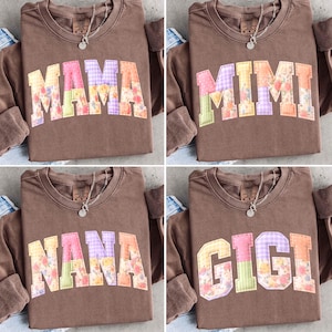 Könnte beinhalten: Vier braune Sweatshirts mit Rundhalsausschnitt, jeweils mit einem anderen Wort: "MAMA", "MIMI", "NANA" und "GIGI". Die Namen sind mit floralem und gemustertem Stoff appliziert. Jedes Shirt hat eine silberne Halskette.