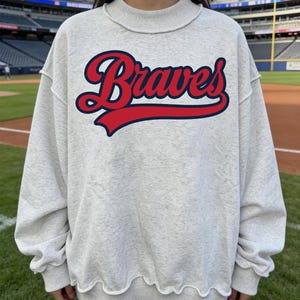 Op de afbeelding: Een witte keramische mok met een zwart handvat en de tekst "But First, Coffee" in een zwarte, vette letter. De mok staat op een wit oppervlak.