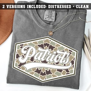 May include: A charcoal gray t-shirt featuring a hexagonal graphic with a camouflage pattern in shades of green, brown, and tan. The word Patriots is printed in white script across the center. The text 2 VERSIONS INCLUDED: DISTRESSED + CLEAN is visible.