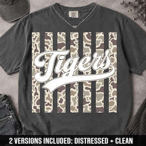 May include: A charcoal gray short-sleeve t-shirt featuring a central graphic of vertical stripes with a camouflage pattern. Overlaid on the stripes is the word Tigers in a large, white, cursive script font. The shirt has a crew neckline.
