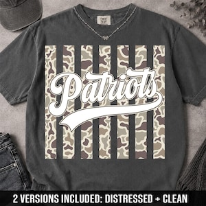 May include: A charcoal gray short-sleeve t-shirt featuring a central graphic of vertical stripes alternating between solid dark gray and a tan, brown, and green camouflage pattern. The word Patriots is printed in large white script across the center.