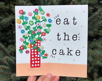 May include: A square white card featuring a red vase with white polka dots containing green stems with colorful small flower embellishments. The text "eat the cake" is printed in black on the right side, with a solid peach-colored horizontal band at the bottom.