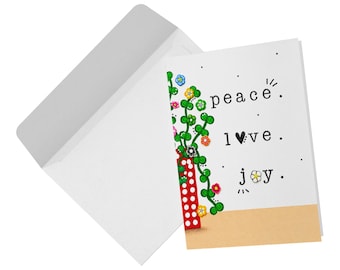 May include: A white greeting card and a matching envelope. The card features a red vase with white dots containing green vines and colorful flowers. The text reads peace, l♥ve, and j✿y, with a tan horizontal band at the bottom of the card.