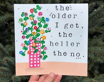 May include: A square greeting card featuring a pink vase with white polka dots, filled with green vines and colorful small flower embellishments. The text reads: the older I get, the heller the no. The card has a light peach base against a pine tree.