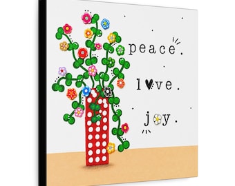 May include: A square wall art piece featuring a red vase with white polka dots containing green stems and colorful flowers. The text reads peace, l♥ve, and j✿y. The background is white with a tan base, and the side edges are black.