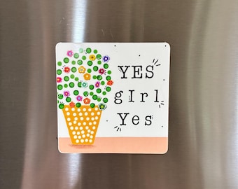 May include: A square refrigerator magnet featuring a potted plant illustration with green leaves and colorful flowers in a yellow polka-dot pot. The text YES gIrL Yes is printed in black on the right side against a white background.