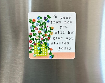 May include: A square refrigerator magnet featuring a green polka-dot pot with trailing vines and colorful flowers. The text reads: a year from now you will be glad you started today. The design is set against a white background with a peach base.