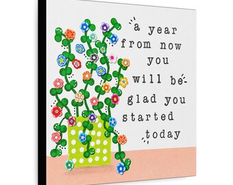 May include: A square canvas wall art piece featuring a green polka-dot pot with trailing green vines and colorful small flowers. The text reads: a year from now you will be glad you started today. The background is white with a peach-colored base.