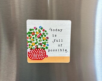 May include: A square refrigerator magnet featuring a red pot with white polka dots filled with colorful flowers. The text reads today is full of possible in a typewriter font against a light background with faint printed text patterns.