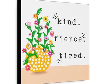 May include: A square wall art piece featuring a yellow polka-dot vase with green stems and colorful small flowers. To the right, the text reads "kind. fierce. tired." in a black typewriter-style font against a white background.